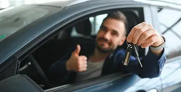 Homem dentro de um carro segurando as chaves do carro e fazendo um simbolo de jóia com as mãos