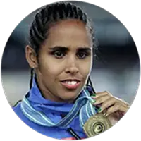 Ex-ginasta Ádria Santos, sorrindo, com uniforme azul e segurando para a câmera uma medalha de ouro pendurada em seu peito.