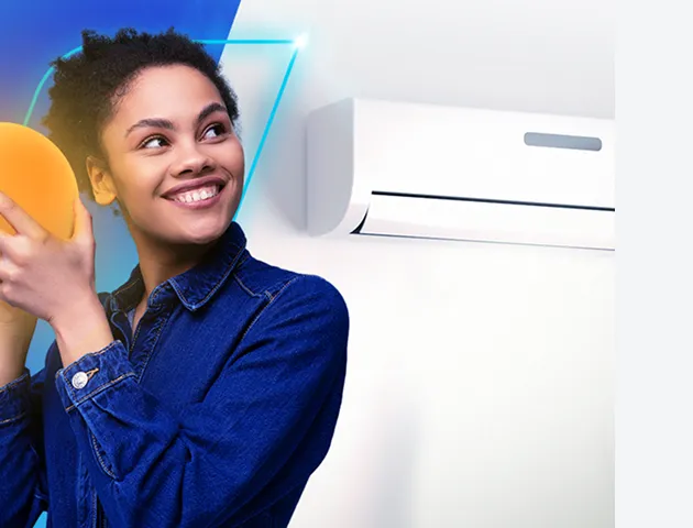 Mulher com camisa jeans, sorrindo. Segura uma esfera de luz amarela e olha para um ar-condicionado na parede.