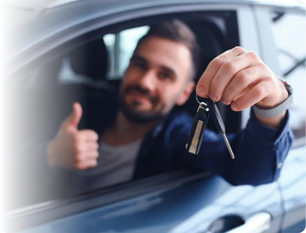 A imagem traz um homem branco, dentro de um carro. Com uma das mãos ele segura uma chave e com a outra faz sinal positivo.