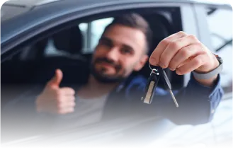 A imagem traz um homem branco, dentro de um carro. Com uma das mãos ele segura uma chave e com a outra faz sinal positivo.