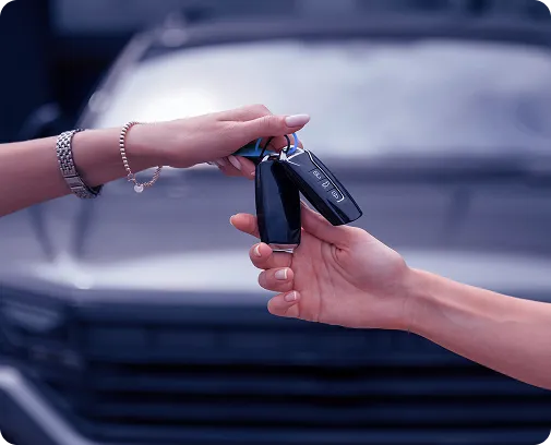 Uma pessoa passando a chave de um carro para outra com o carro ao fundo.