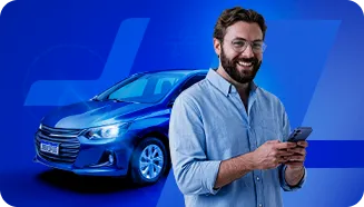 Homem branco em pé, vestindo uma camisa de botão azul-clara, com o celular na mão. Ao fundo, um carro azul.