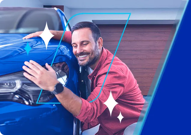 Homem feliz agachado abraçando um automóvel azul em frente uma garagem.