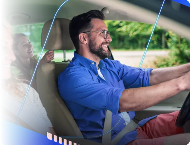 Um homem feliz e sorridente dirigindo um carro, com uma mulher no banco de passageiro e outra no banco traseiro, felizes.