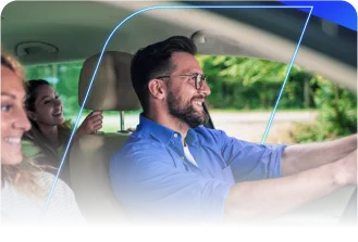 Um homem feliz e sorridente dirigindo um carro, com uma mulher no banco de passageiro e outra no banco traseiro, felizes.