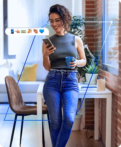 Mulher sorrindo em um escritório, usa o celular e segura uma caneca. Uma faixa de emojis sai do aparelho.