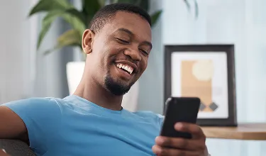 Homem sorridente sentado no sofá olhando o celular