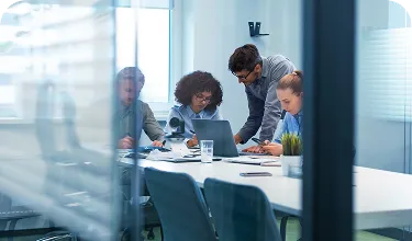 Em uma sala de reunião, pessoas conversam enquanto olham o computador.