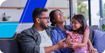 Família sentada no sofá a conversar e sorrir em sala iluminada com janelas ao fundo