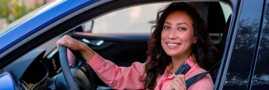 Mulher alegre e sorridente no volante de um carro, enquanto segura uma chave.