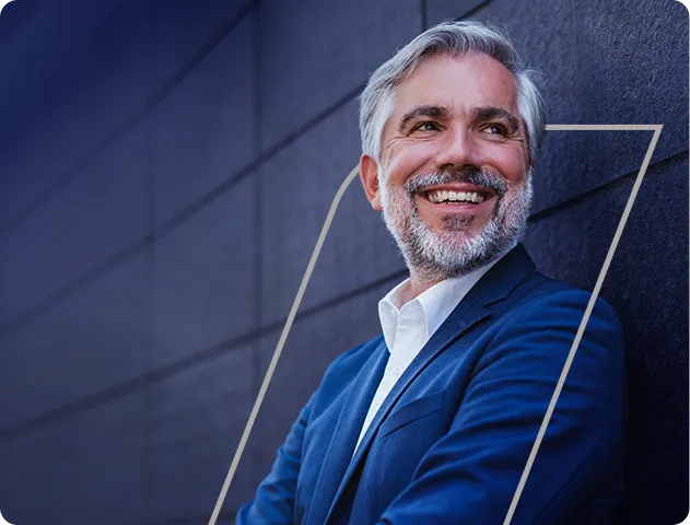 Na imagem, temos um homem executivo em pé, encostado em uma parede.