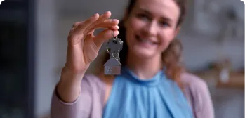 Mulher sorrindo e segurando uma chave com um chaveiro em formato de casa.