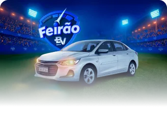 Um carro branco com farol acesso em um estádio de futebol e acima dele um selo escrito Feirão BV.