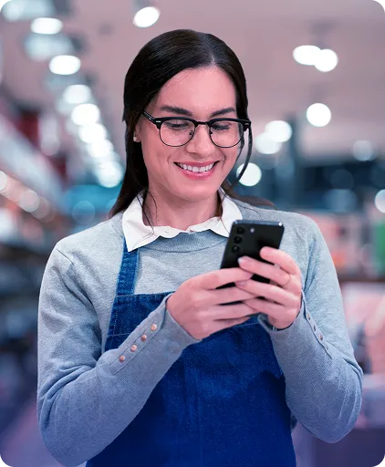 Uma mulher sorrindo está segurando um celular com as duas mãos.