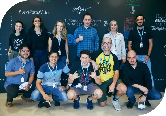 Homens e mulheres, colaboradores do banco BV, lado a lado, alguns estão em pé, outros estão agachados, posando para a foto.