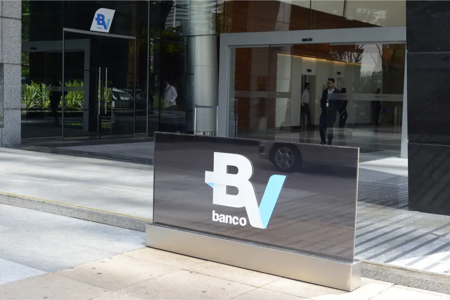 Entrada do prédio toda em vidro. Em primeiro plano, o logo do banco BV.