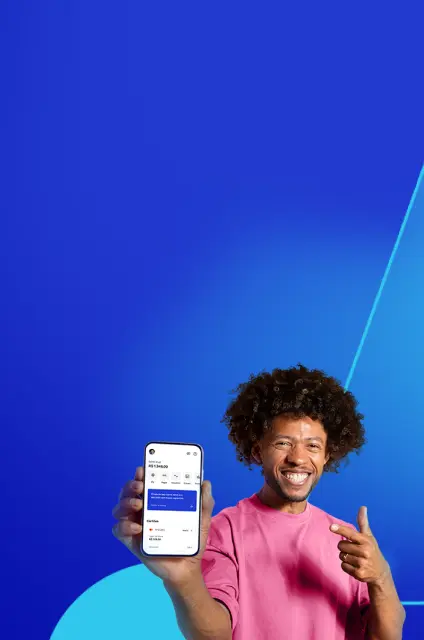 Um homem de camiseta rosa, cabelo black e sorrindo. Com uma mão, ele mostra a tela de um smartphone e aponta com a outra.