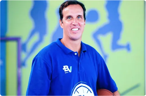 Marcelinho Machado, líder do projeto M4 nas Escolas, segurando uma bola de basquete e vestindo uma camisa polo azul.