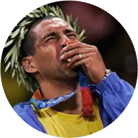 Ex-jogador de vôlei Serginho, com uma coroa de louros, beijando a medalha olímpica, olhando para cima e chorando.