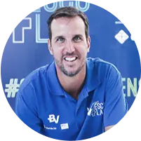 Ex-jogador de basquete Marcelinho Machado sorrindo, de camiseta polo azul com logos do banco BV e Instituto M4 nas Escolas.