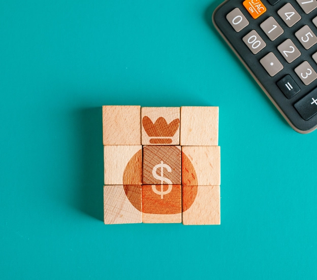 Blocos de madeira formando um ícone de saco de dinheiro ao lado de uma calculadora sobre fundo verde, representando planejamento financeiro para conseguir melhor redução de juros de empréstimo com Open Finance.