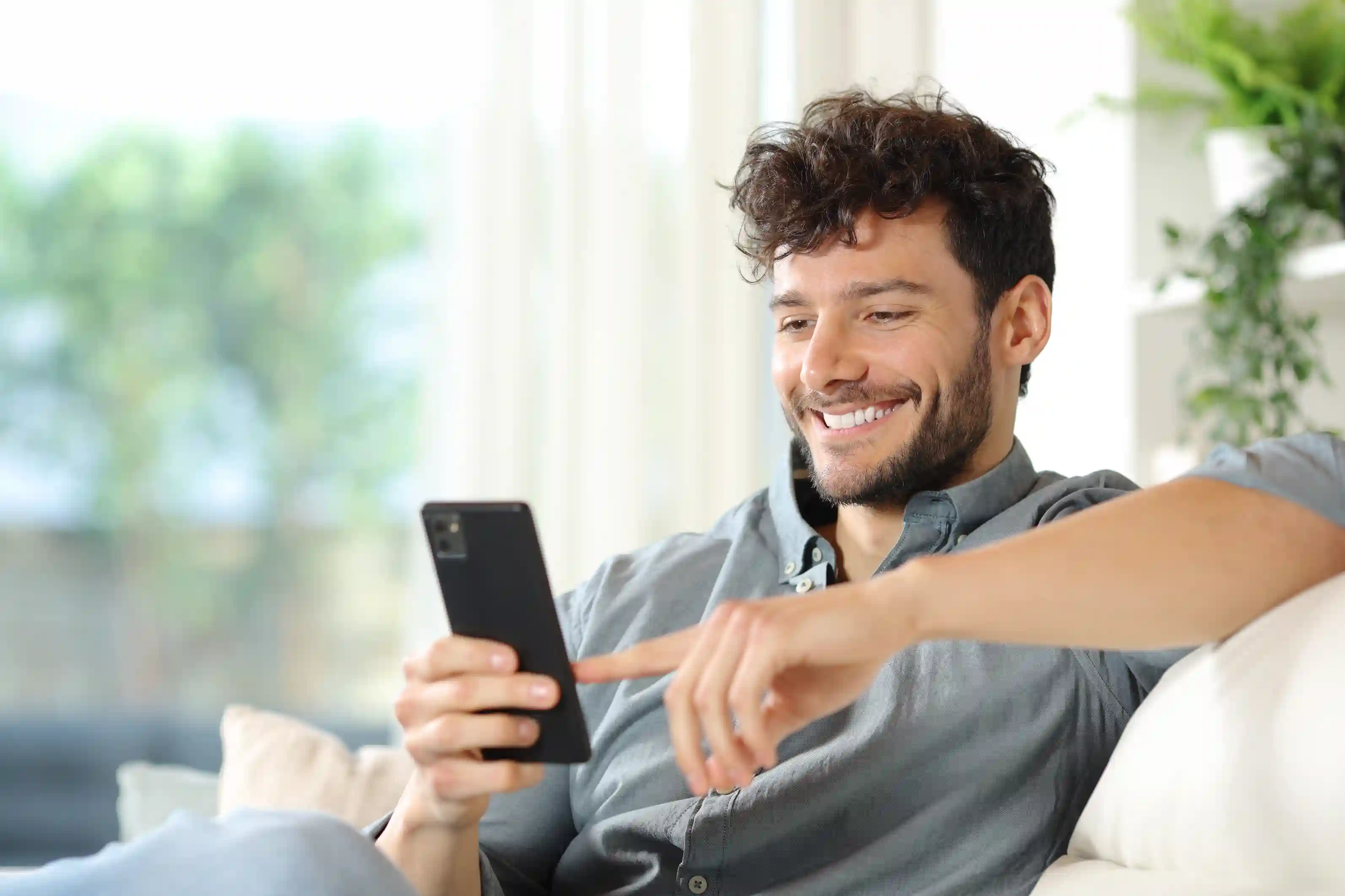 homem sentando no sofá sorrindo mexendo no celular