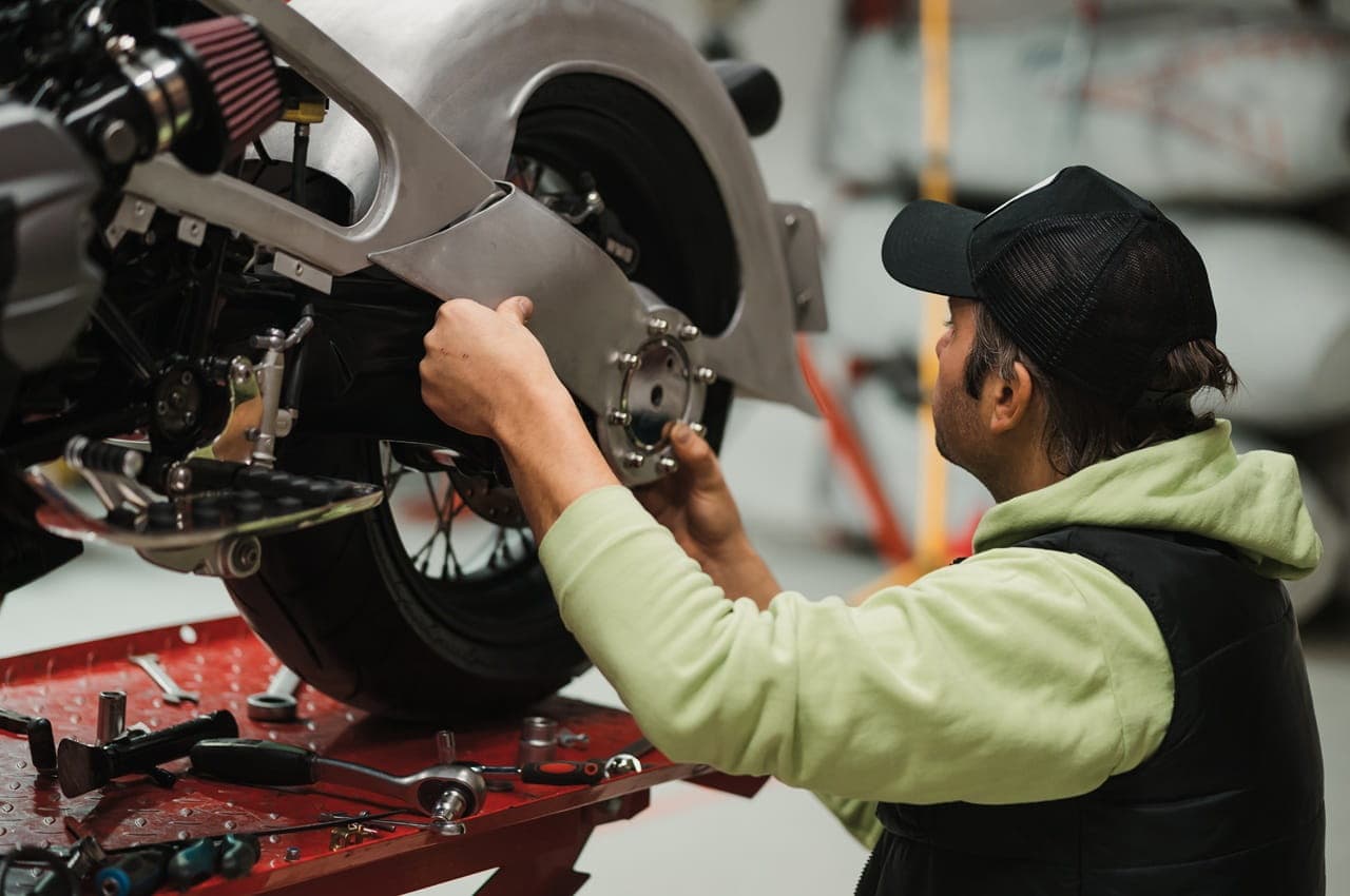Mecânico fazendo a manutenção da roda traseira de uma motocicleta que está sobre uma plataforma elevatória vermelha, com ferramentas.