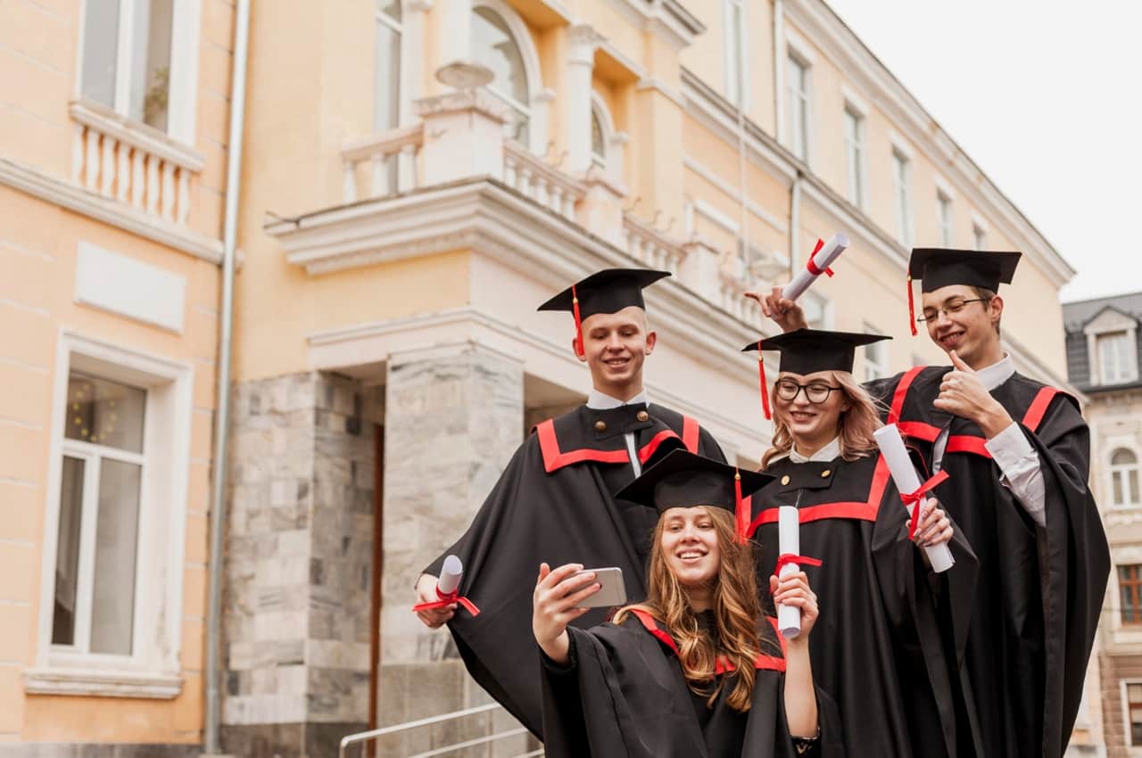 Jovens com beca e capelo segurando um diploma universitário na formatura.