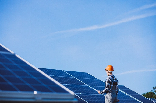 Imagem de um homem, utilizando um uniforme e capacete de segurança, enquanto trabalha com placas solares.